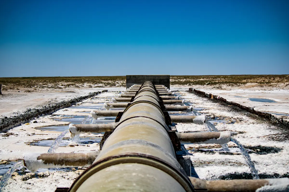 Brine flowing from pipe outlets across a white salt-crusted flat in dry scrubland