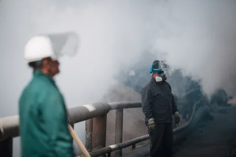 Workers in hard hats and respirators in a cloud of smoke
