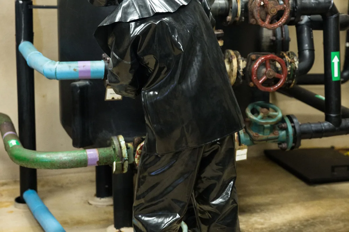 Worker in a chemical protective suit next to gas piping and valves