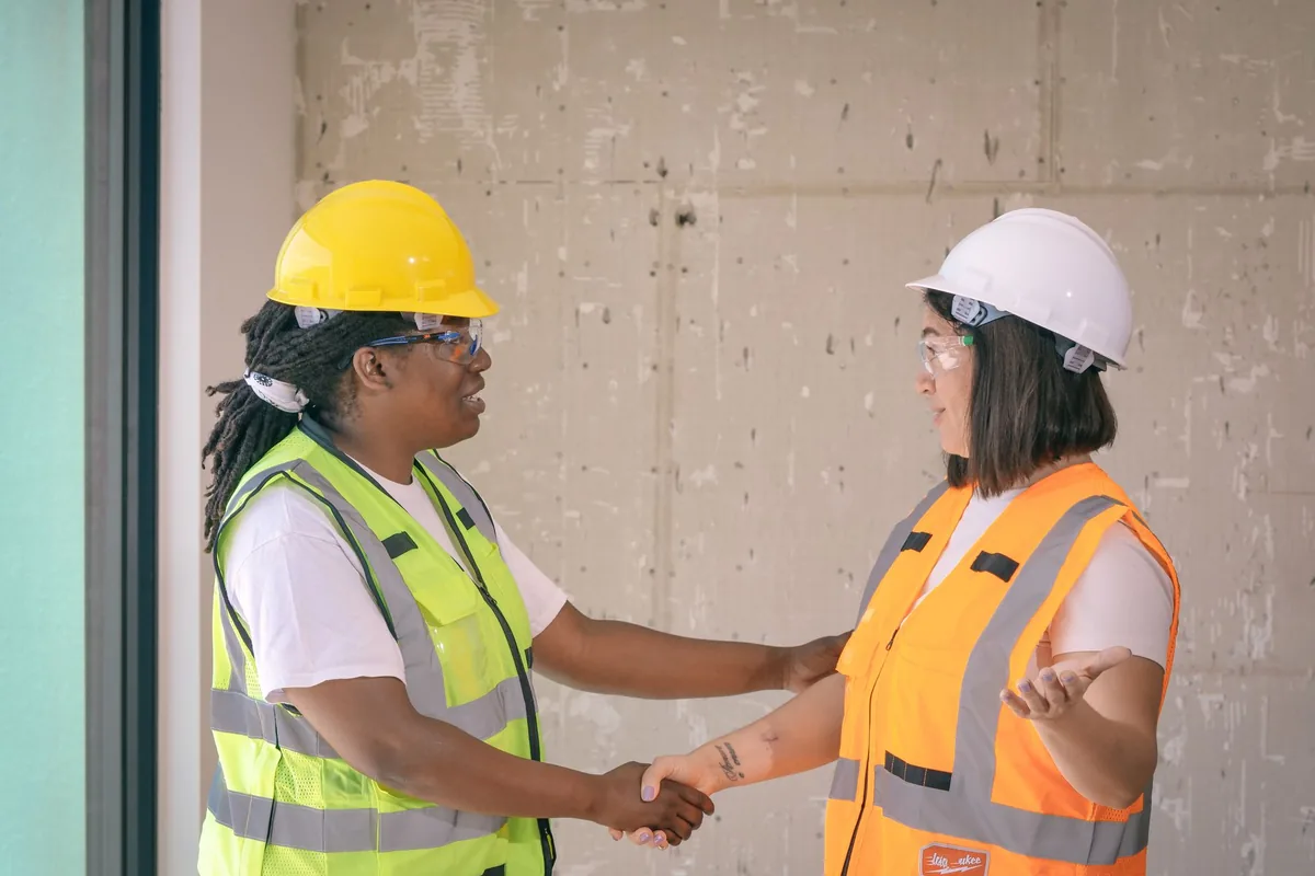 Two workers in hard hats and safety vests shaking hands