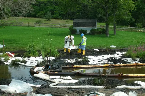 Cleanup crew in protective gear working an oil spill with absorbent pads and booms