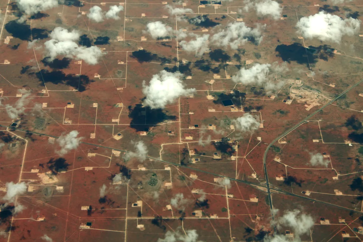 Aerial view of Permian Basin well pads, caliche lease roads and pipeline right-of-way corridors near Midland, Texas