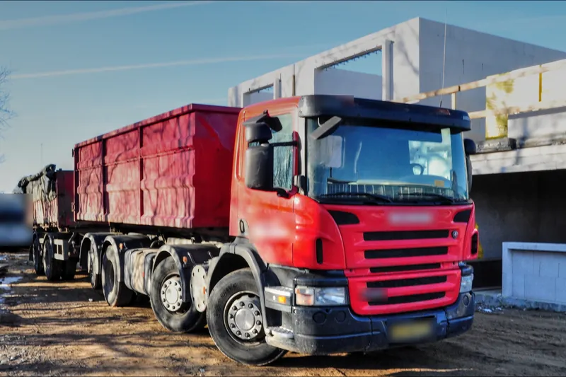 Roll-off truck and trailer hauling loaded containers on a dirt job site